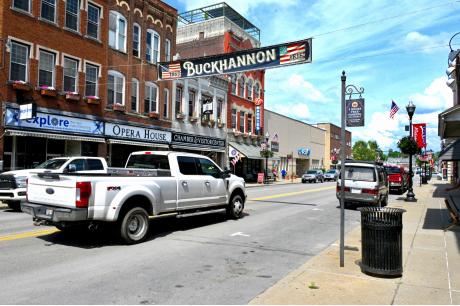 Downtown street in Buckhannon, West Virginia, with brick storefronts, parked vehicles, and a large “Buckhannon” banner hanging above the road.