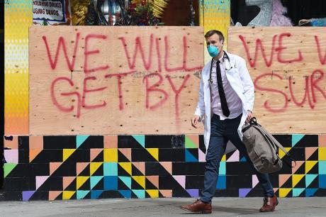 Masked doctor walks past a boarded building