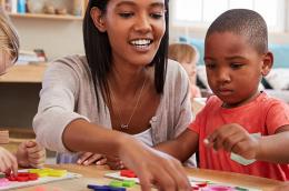 female teacher working at classroom table with four prekindergarten students