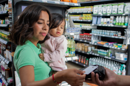 A mother holding her baby pays for food at the store.