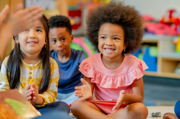 Two young children listen to their instructor and happily clap along. 