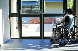 Photo of a woman in a wheelchair looking outside the glass doors of a medical facility. 
