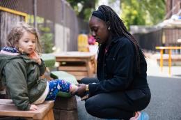 A child care worker squats to put shoes on a child.