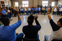 About two dozen incarcerated women sit in chairs arranged in a circle in a classroom. Some raise their hands.  