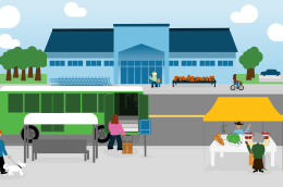 City street with a bus stop, farmers' market stall, and people walking, biking, and sitting near a large grocery store.