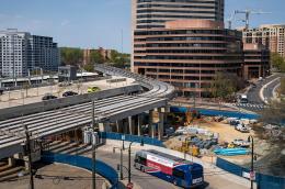 A bus drives under an underpass and beside a construction area