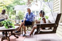 A grandfather, grandmother, and granddaughter sit on a front porch
