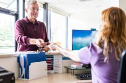 A man reaches forward and hands a card to a receptionist at a doctor's office