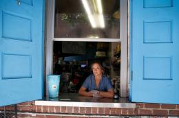 A woman working in a restaurant looks out a carry-out window at the camera