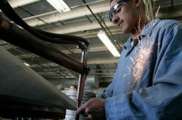 A man wearing safety glasses and a blue uniform works in a factory