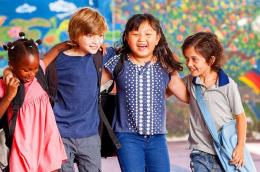 Four elementary school age children hold each other around the shoulders while walking and smiling