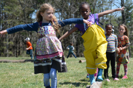 Two children play together outside, one walks on a balance beam