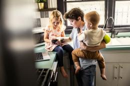 A parent working on a laptop while caring for two children.