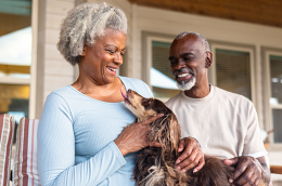 An older Black man and woman sit on a porch holding their dog