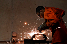 A man wearing an orange jumpsuit uses a tool, sparks fly