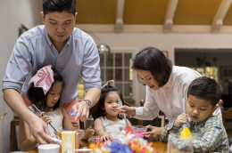 A young Asian​ family is making glittered slime for arts and craft at home during their leisure time. The picture shows the mother and father helping the children get their hands on making slime.