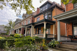 Row of historic brick houses with columned porches and a garden in front.