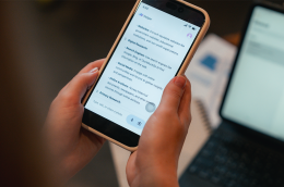 A person holds a smartphone displaying an “AI Helper” chat screen