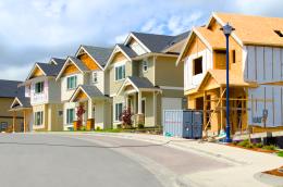 Two completed houses sit between two undergoing construction on a new-feeling residential street.