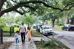 Image of a young Black father smiling and walking his kids down the street.