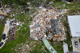 Aerial view of a neighborhood showing severe storm damage, with one home reduced to debris and wreckage scattered across surrounding yards.