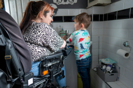 Image of a young disabled woman in a wheelchair helping her son wash his hands in the bathroom sink.