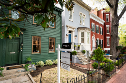 Several row houses, one with a Compass realty sign in the small front yard