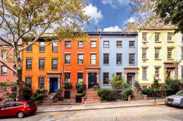A street-level shot of colorful rowhomes along a cobblestone road on a bright but cloudy day.