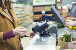 A woman in a camel-colored jacket pays with a credit card at the grocery store check-out.