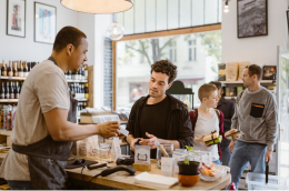 People shopping at a neighborhood store while a cashier assists a customer at the checkout counter.