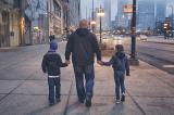 photo of father holding hands with children walking on sidewalk