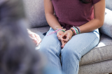 A cropped image of women sitting on a couch with her hands on her lap.