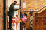 photo of elementary school teacher greeting his students at the door with a high-five
